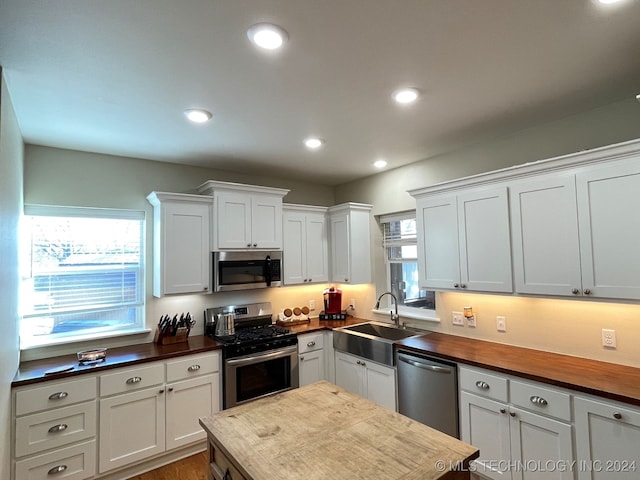 kitchen with appliances with stainless steel finishes, white cabinetry, sink, and butcher block countertops