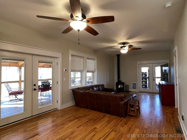 living room with a wood stove, ceiling fan, wood-type flooring, and french doors