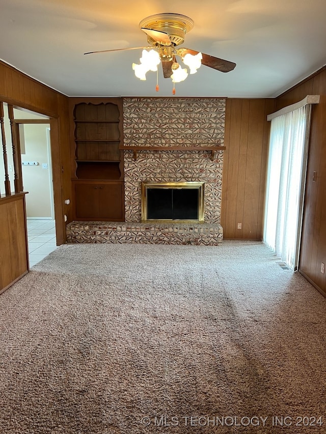 unfurnished living room featuring ceiling fan, a large fireplace, carpet, and wooden walls