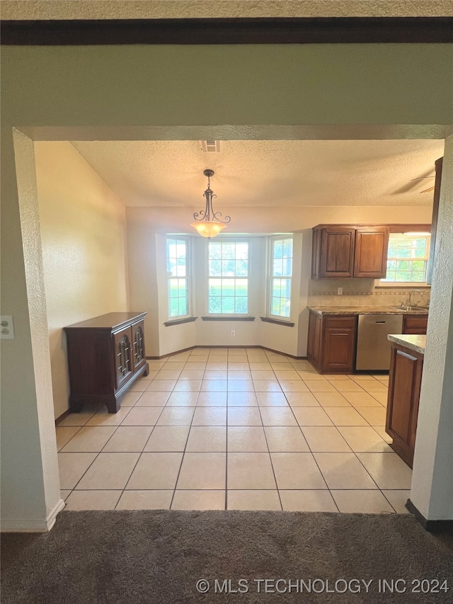 kitchen featuring a textured ceiling, decorative light fixtures, a notable chandelier, light tile patterned floors, and stainless steel dishwasher