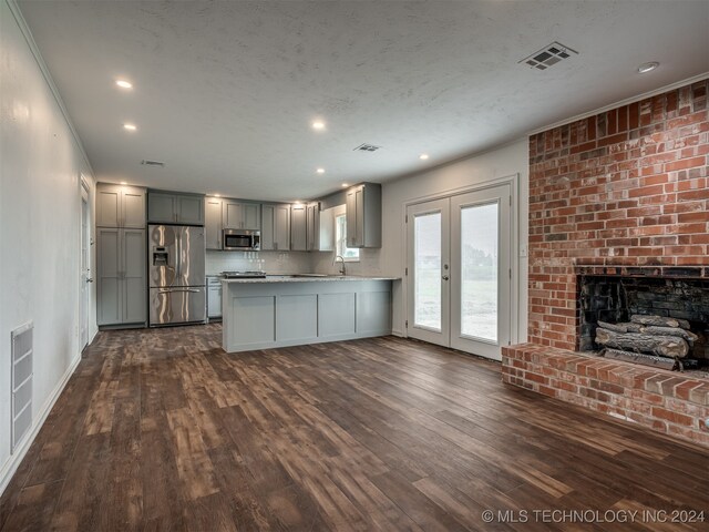 kitchen with stainless steel appliances, dark hardwood / wood-style floors, gray cabinetry, kitchen peninsula, and a brick fireplace