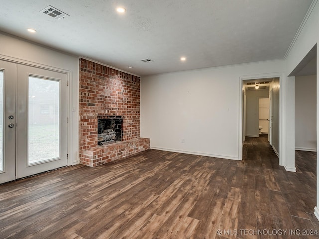 unfurnished living room featuring brick wall, hardwood / wood-style floors, french doors, a fireplace, and crown molding