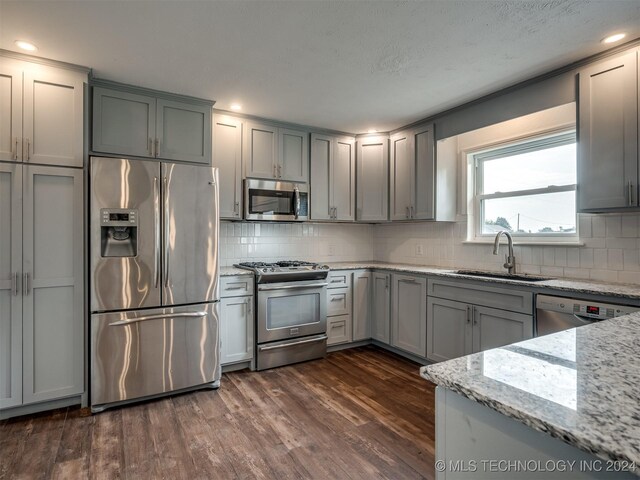 kitchen with decorative backsplash, dark hardwood / wood-style floors, appliances with stainless steel finishes, light stone counters, and sink