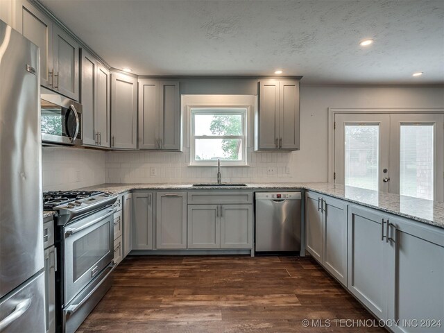 kitchen with sink, appliances with stainless steel finishes, decorative backsplash, light stone countertops, and dark hardwood / wood-style floors