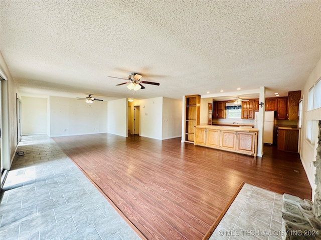 living room with a textured ceiling, light hardwood / wood-style flooring, ceiling fan, and a healthy amount of sunlight