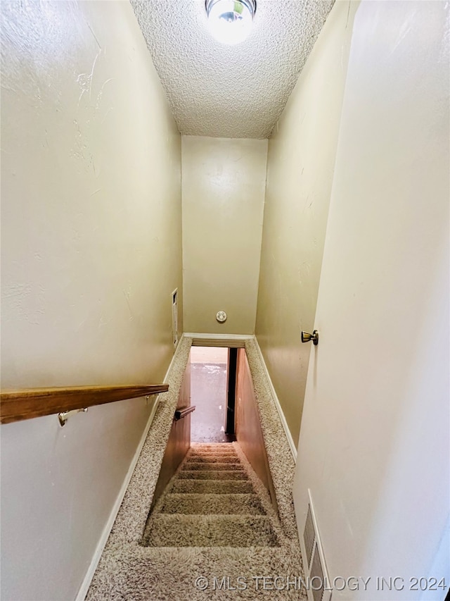 stairway with carpet and a textured ceiling