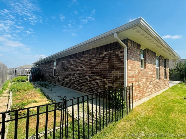 view of side of home with a yard, a fenced backyard, and brick siding