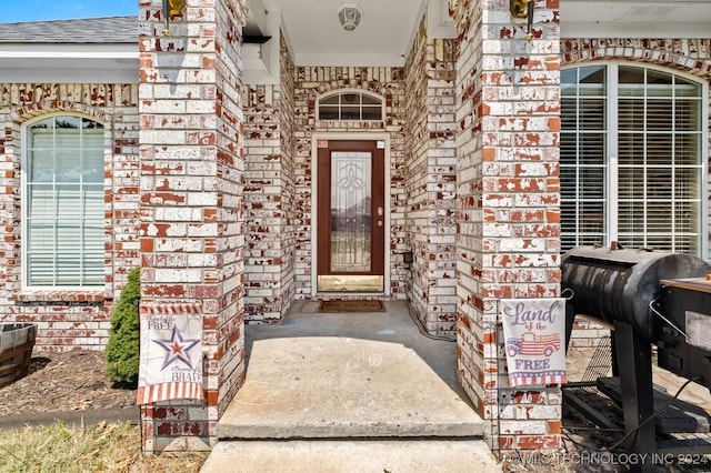 view of exterior entry featuring brick siding and roof with shingles