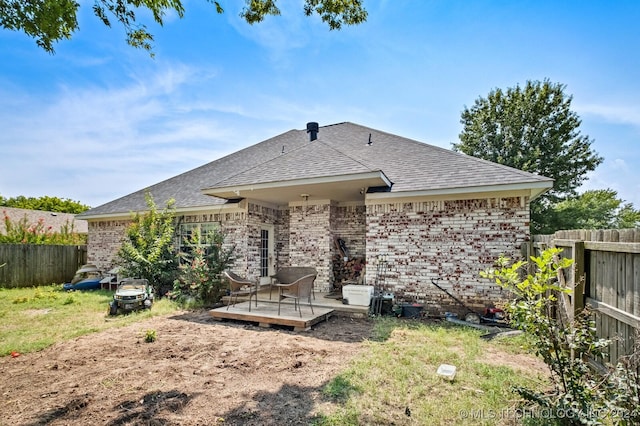 rear view of property with roof with shingles, brick siding, a fenced backyard, and a wooden deck