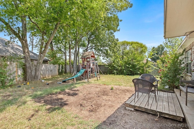 view of yard with a deck, a playground, and a fenced backyard