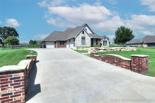 view of front facade with a front yard, fence, a garage, stone siding, and driveway