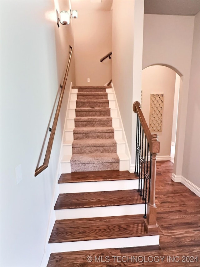 stairs featuring arched walkways, wood finished floors, and baseboards