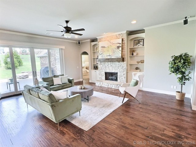 living room featuring dark wood-style floors, baseboards, crown molding, and a stone fireplace