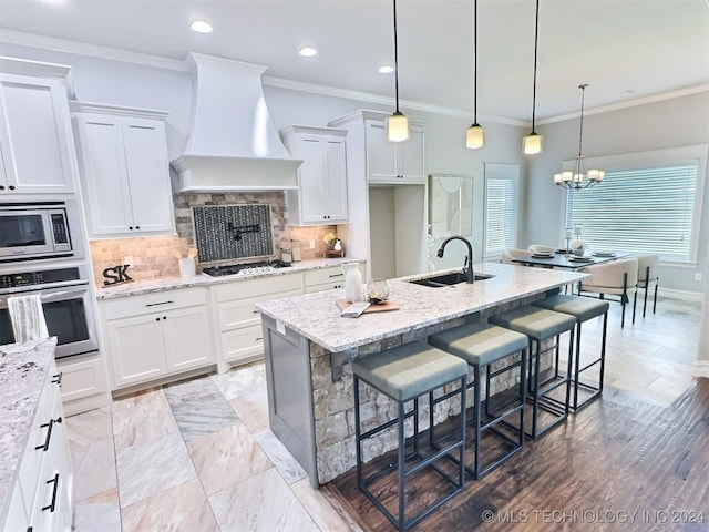 kitchen featuring a breakfast bar area, custom exhaust hood, stainless steel appliances, white cabinetry, and a sink