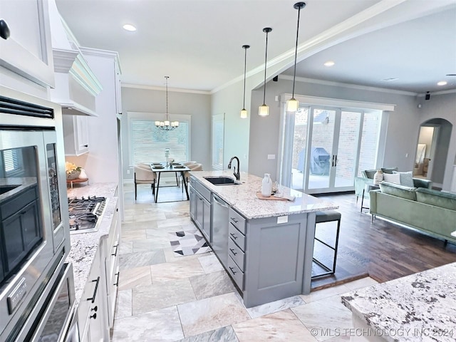 kitchen with a kitchen island with sink, a sink, white cabinetry, appliances with stainless steel finishes, and pendant lighting