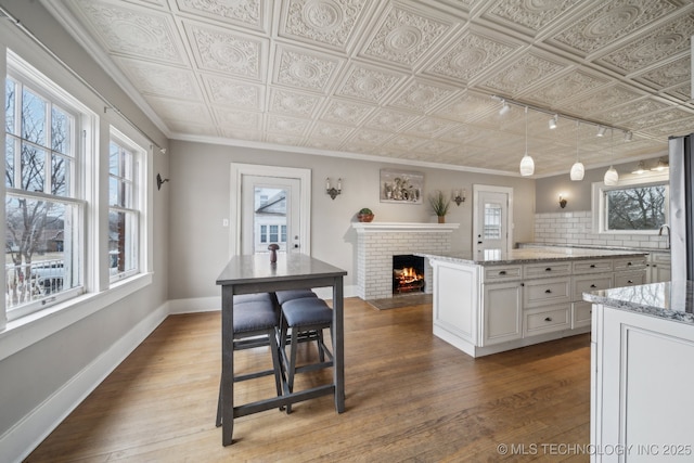 kitchen with hardwood / wood-style floors, white cabinets, hanging light fixtures, light stone countertops, and a brick fireplace