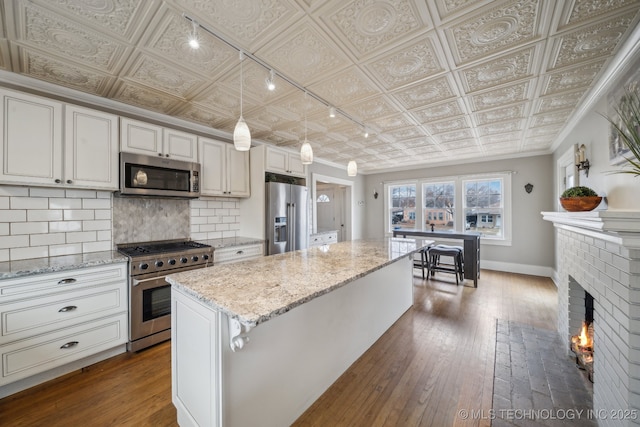 1715 Grandview Ave, Pawhuska, OK 74056 - kitchen featuring appliances with stainless steel finishes, an ornate ceiling, decorative backsplash, dark wood-type flooring, and a kitchen island