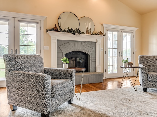 living room featuring vaulted ceiling, plenty of natural light, a brick fireplace, and french doors