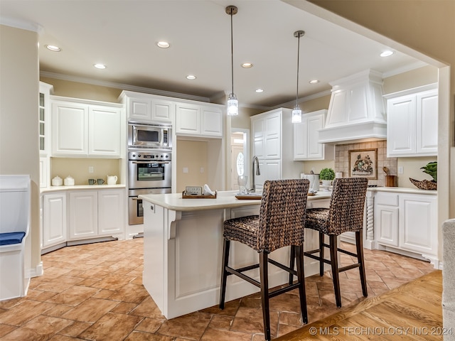 kitchen featuring decorative light fixtures, a center island with sink, appliances with stainless steel finishes, a kitchen bar, and white cabinetry