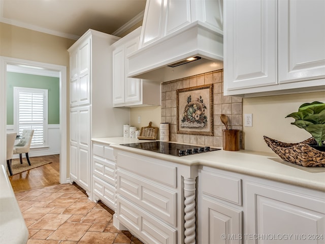 kitchen with custom range hood, ornamental molding, black electric cooktop, light wood-type flooring, and white cabinets