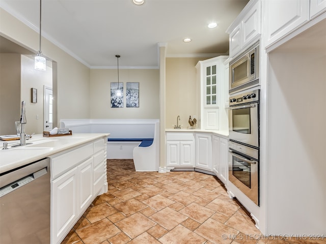 kitchen with hanging light fixtures, appliances with stainless steel finishes, white cabinetry, sink, and ornamental molding