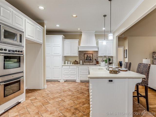 kitchen featuring hanging light fixtures, white cabinetry, sink, a kitchen island with sink, and a breakfast bar