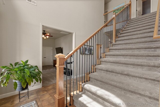 stairway with ceiling fan, a high ceiling, and tile patterned flooring