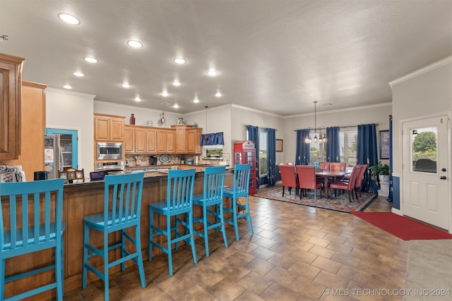 kitchen featuring stainless steel appliances, an inviting chandelier, tile patterned flooring, crown molding, and a breakfast bar area