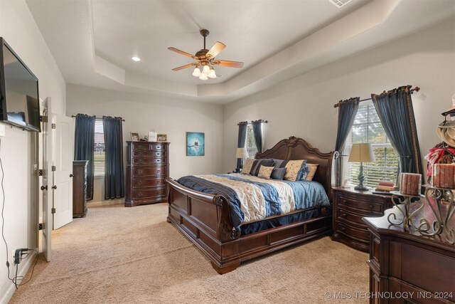 bedroom with ceiling fan, light carpet, and a raised ceiling