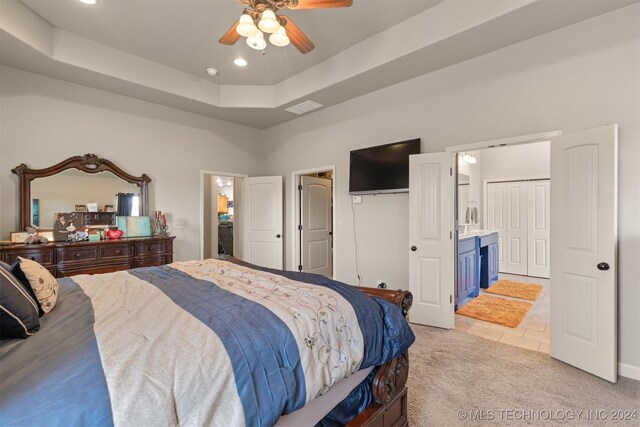 bedroom with ceiling fan, a raised ceiling, light colored carpet, and ensuite bath