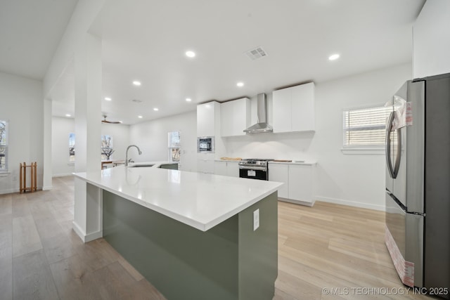 kitchen with sink, stainless steel appliances, light hardwood / wood-style floors, white cabinets, and wall chimney exhaust hood