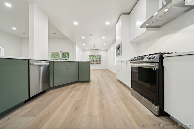 kitchen featuring wall chimney range hood, green cabinets, stainless steel appliances, light hardwood / wood-style floors, and white cabinets