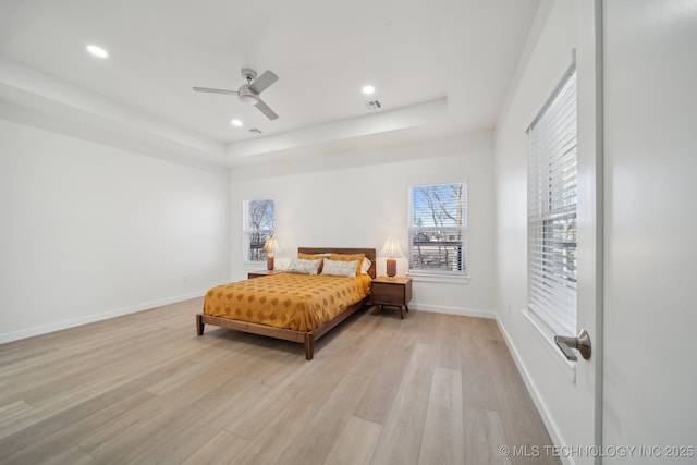 bedroom featuring light wood-type flooring, ceiling fan, and a tray ceiling