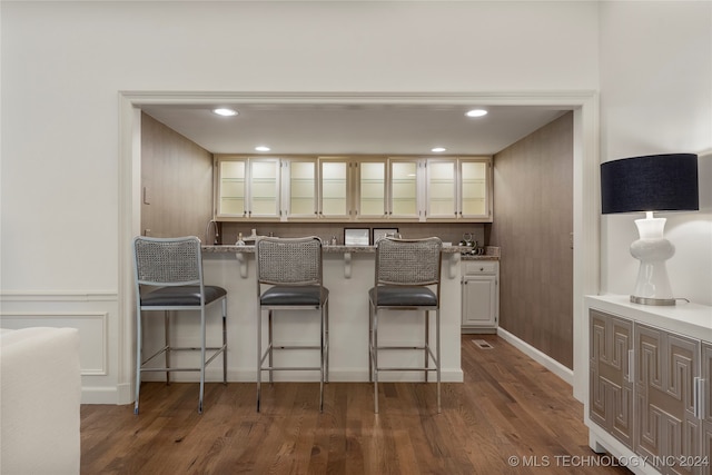 kitchen with hardwood / wood-style floors, a kitchen bar, light stone countertops, white cabinets, and kitchen peninsula