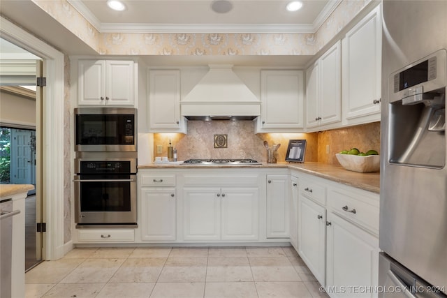 kitchen featuring appliances with stainless steel finishes, backsplash, white cabinetry, ornamental molding, and custom exhaust hood