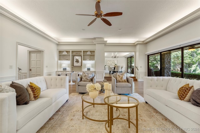 living room with ceiling fan with notable chandelier, crown molding, light hardwood / wood-style flooring, and built in shelves