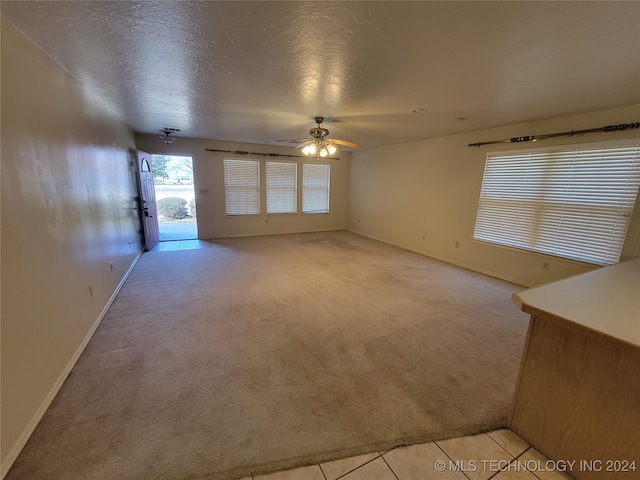 unfurnished living room featuring a textured ceiling, ceiling fan, and light carpet