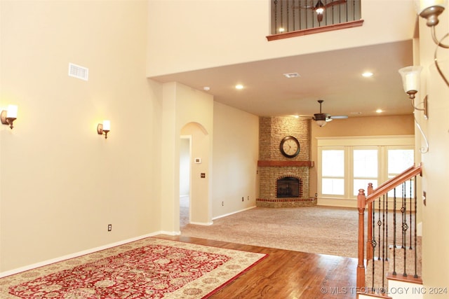 carpeted living room featuring a high ceiling, brick wall, ceiling fan, and a brick fireplace