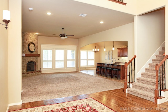 unfurnished living room with ceiling fan with notable chandelier, light colored carpet, a brick fireplace, and a healthy amount of sunlight