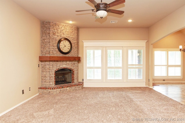 unfurnished living room with carpet flooring, ceiling fan, brick wall, and a stone fireplace