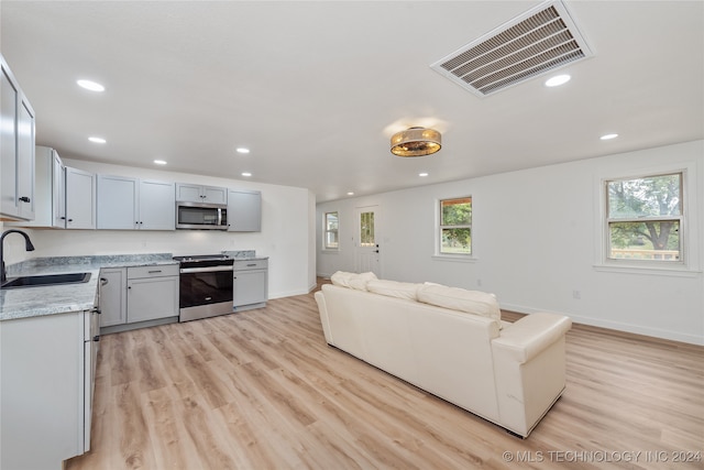 kitchen featuring light wood-type flooring, appliances with stainless steel finishes, light stone counters, and sink