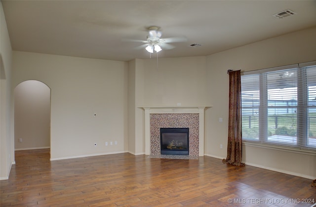 unfurnished living room featuring ceiling fan, a tiled fireplace, and hardwood / wood-style flooring