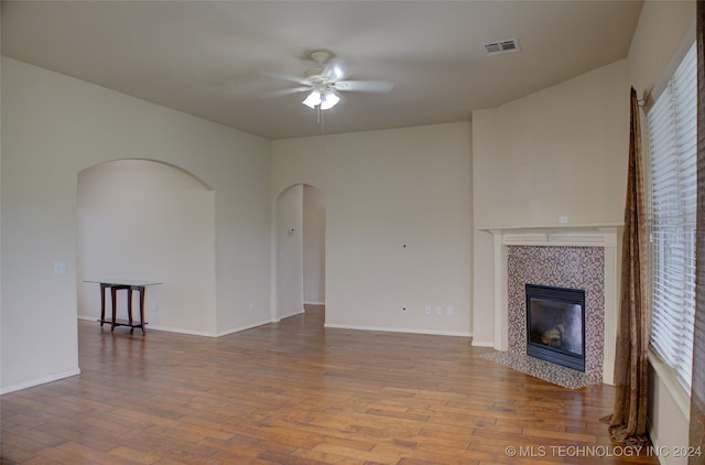 unfurnished living room with ceiling fan, a tiled fireplace, and hardwood / wood-style floors