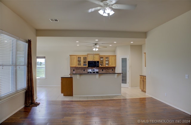 kitchen featuring light hardwood / wood-style flooring, kitchen peninsula, ceiling fan, decorative backsplash, and a breakfast bar