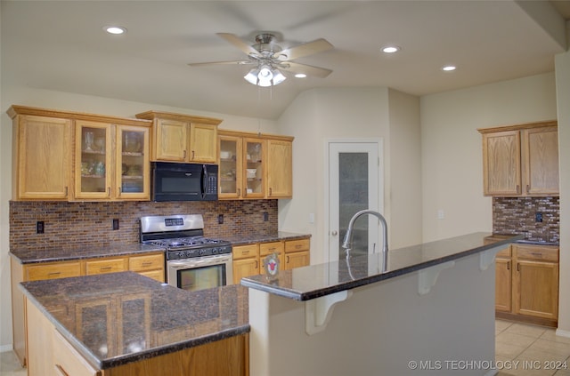 kitchen with an island with sink, gas range, ceiling fan, and a kitchen bar