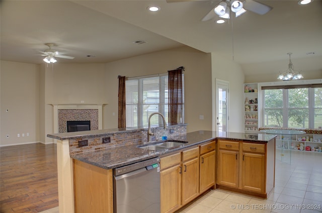 kitchen with light wood-type flooring, ceiling fan with notable chandelier, a tiled fireplace, sink, and stainless steel dishwasher