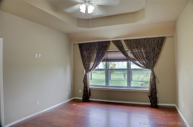 unfurnished room featuring a raised ceiling, wood-type flooring, and ceiling fan