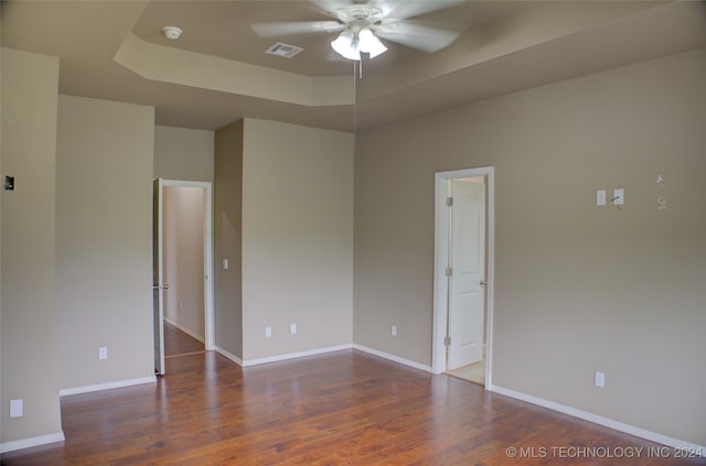 empty room with ceiling fan, dark hardwood / wood-style floors, and a raised ceiling