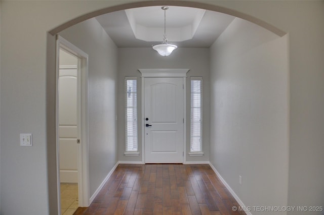 entrance foyer with arched walkways, a tray ceiling, dark wood finished floors, and baseboards