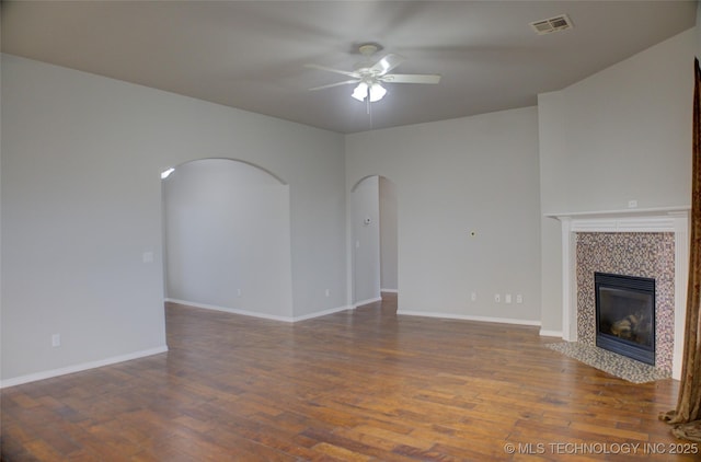 unfurnished living room with arched walkways, a fireplace, ceiling fan, wood finished floors, and baseboards